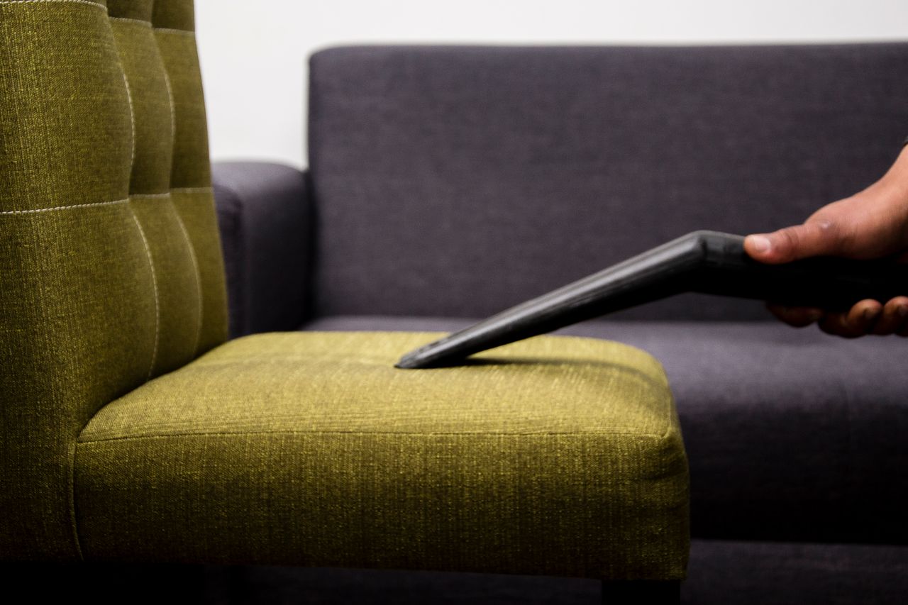 Gros plan d’une personne aspirant un fauteuil sofa moderne en intérieur, mettant en avant un service de nettoyage.